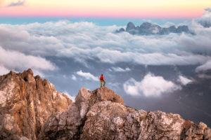 Lonely man stands on top of a mountain ridge, on the background a sea of clouds around the Agner mountain range, Pale di San Martino group, view from Costabella ridge, Dolomites, Italy Lonely man stands on top of a mountain ridge, on the background a sea of clouds around the Agner mountain range, Pale di San Martino group, view from Costabella ridge, Dolomites, Italy